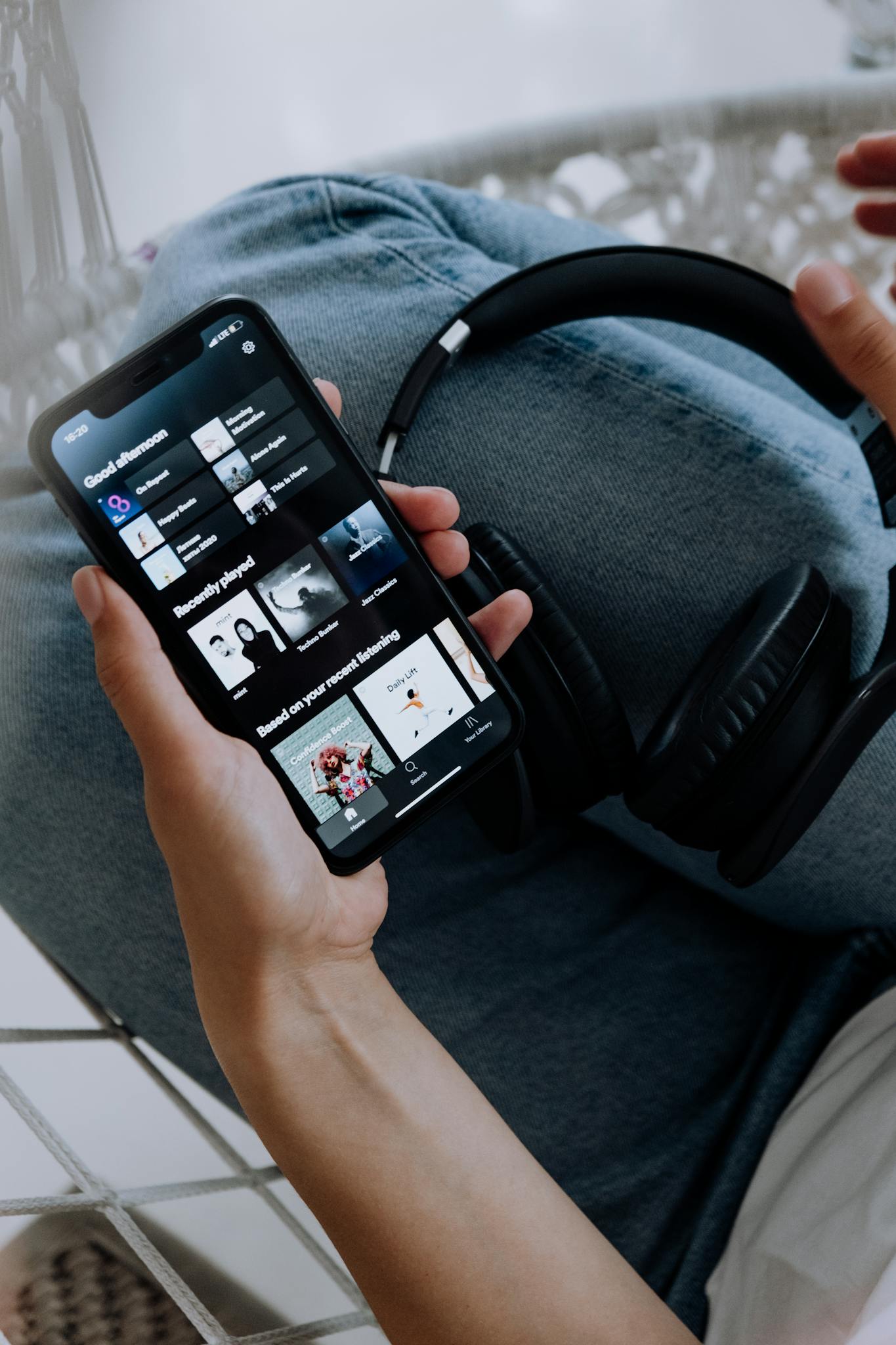 Close-up of a person holding a smartphone with headphones, browsing a music app.